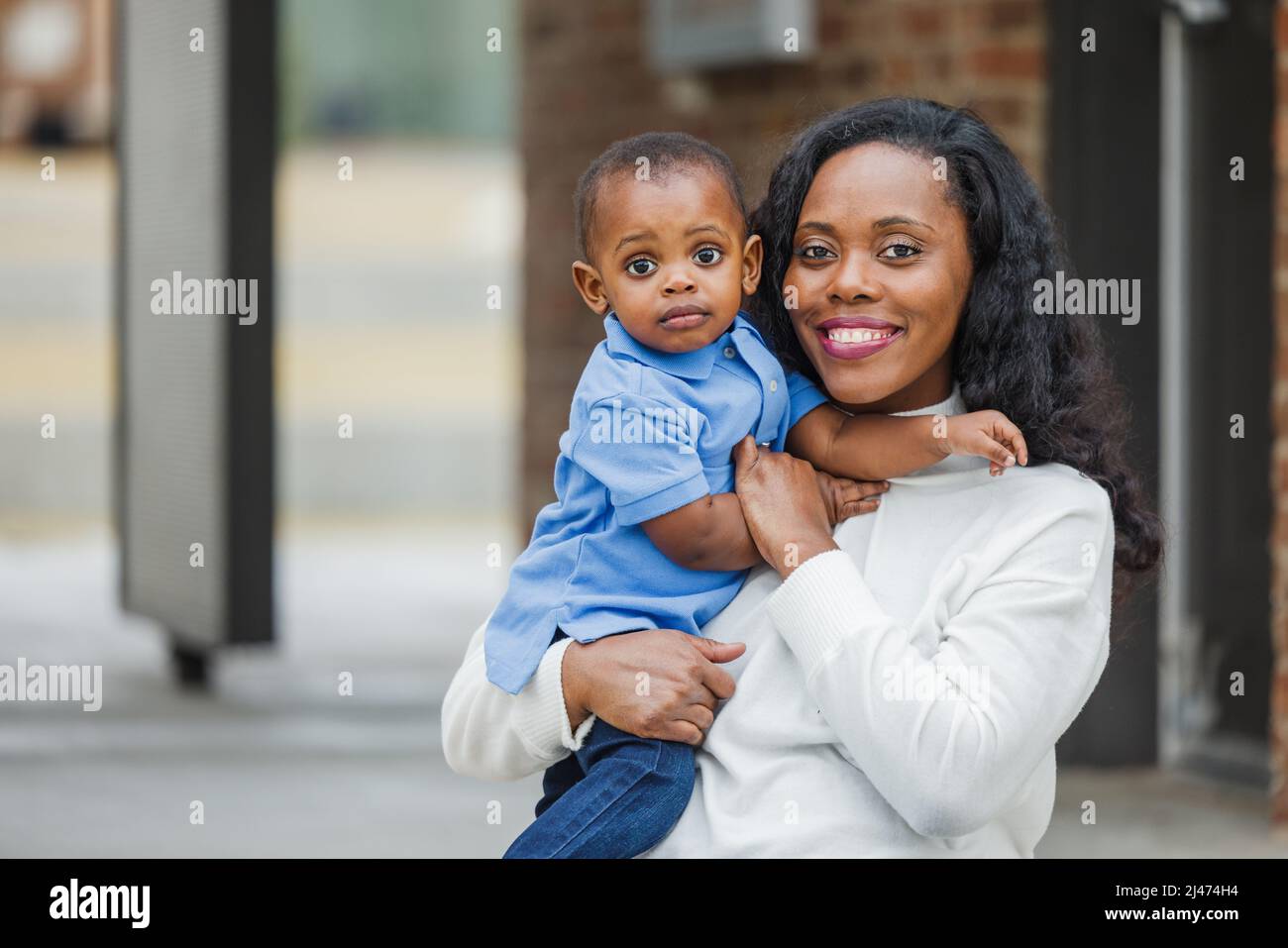 Eine schöne afroamerikanische Mutter, die draußen auf einer Treppe sitzt und ihren kleinen Jungen in der Hand hält, sieht traurig aus Stockfoto