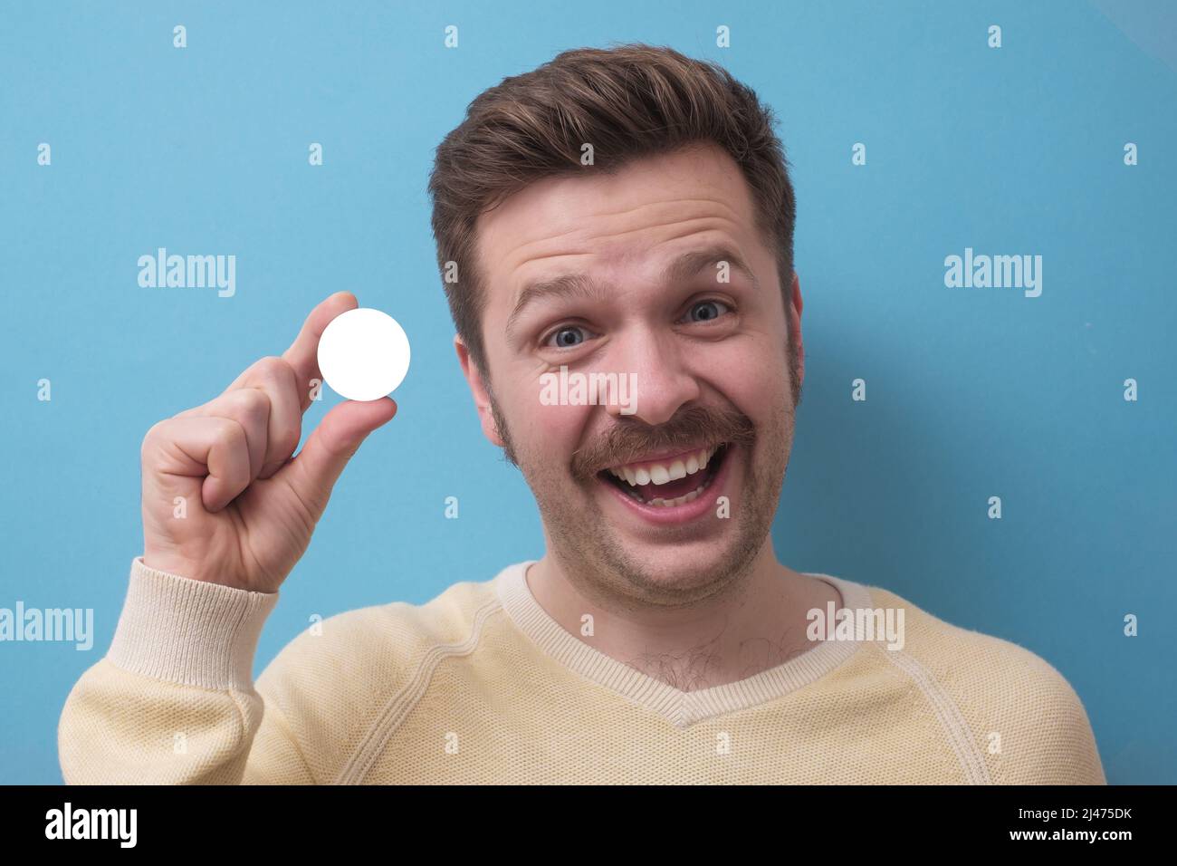 Mann mit Schnurrbart Blick auf Kamera Holdin g in den Fingern weißen Kreis als Copyspace. studio auf blaue Wand aufgenommen. Stockfoto