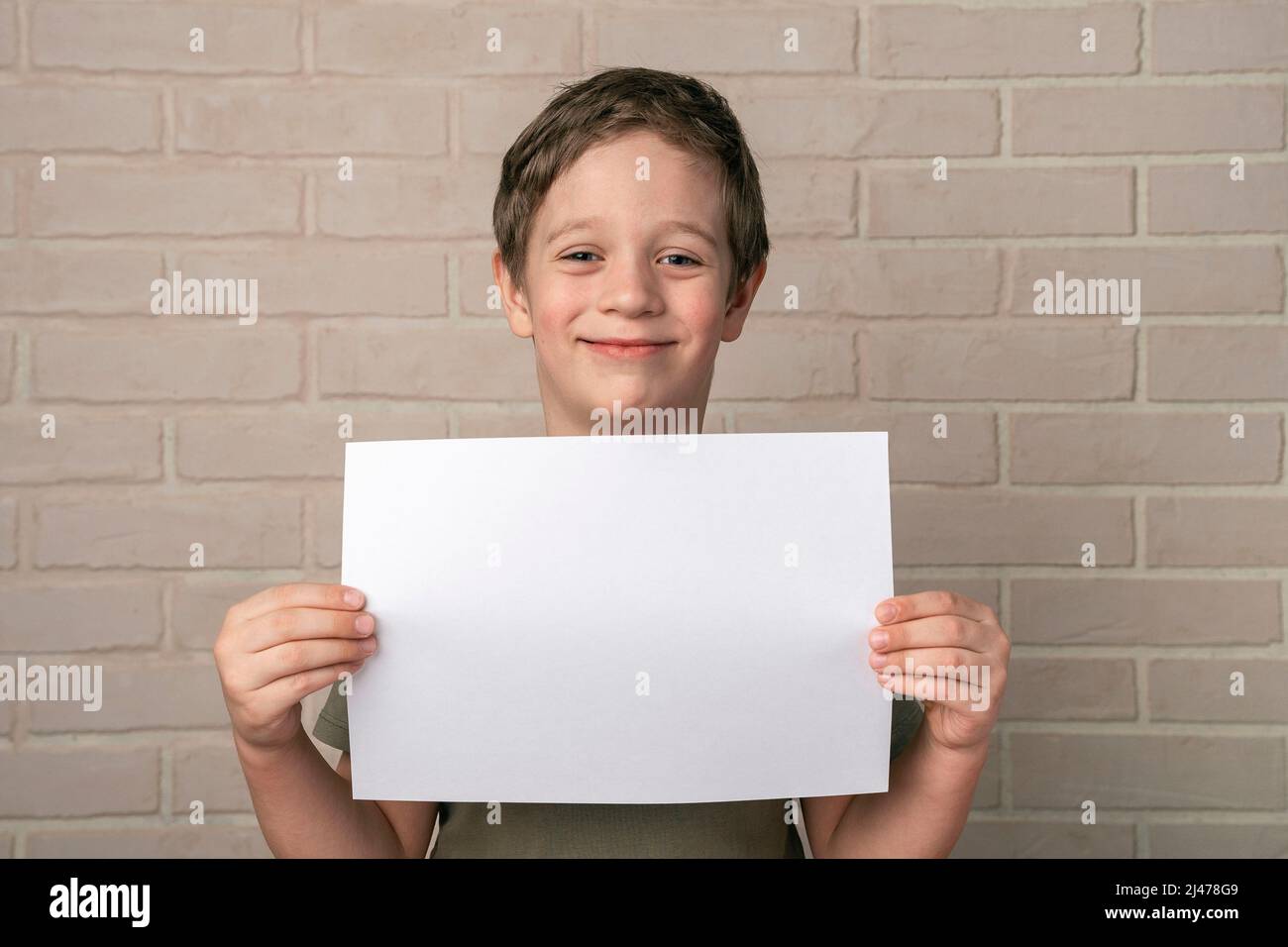 Ein fröhlich lächelnder 5-jähriger europäischer Junge hält ein leeres Plakat über seinem Kopf Stockfoto