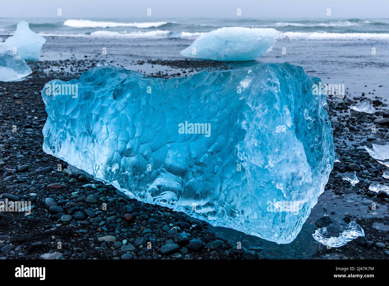Ozeanwellen brechen über Eisberge und große Stücke blauen Eises an einem vulkanischen schwarzen Sandstrand (Diamond Beach, Island) Stockfoto