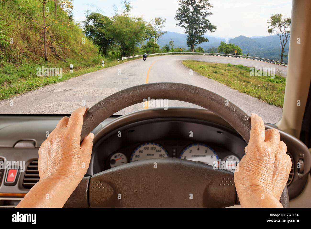 Ältere Frau, die ein Auto langsam auf der Bergstraße fährt. Stockfoto