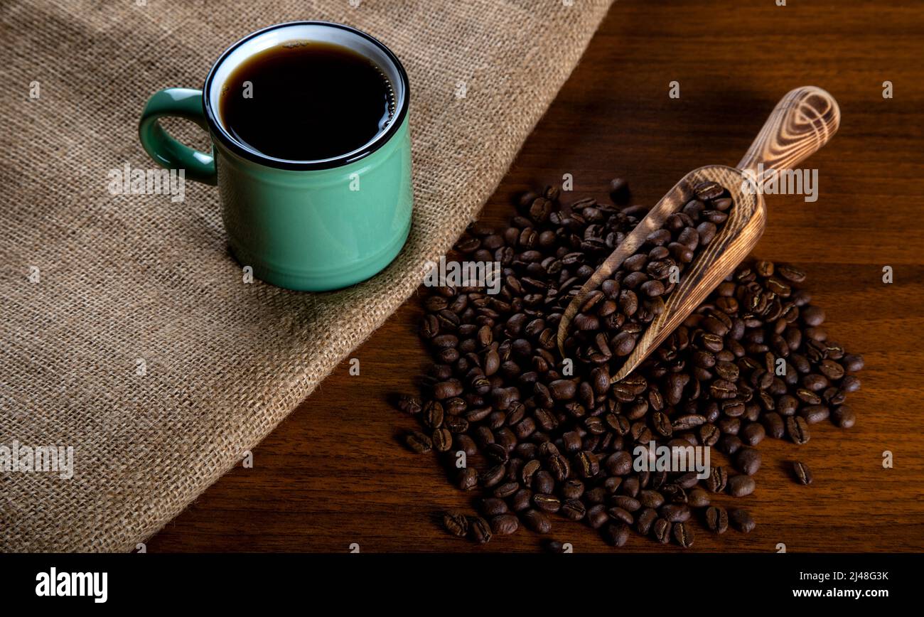 Grüne Tasse Kaffee mit Kaffeebohnen auf Holzhintergrund Stockfoto
