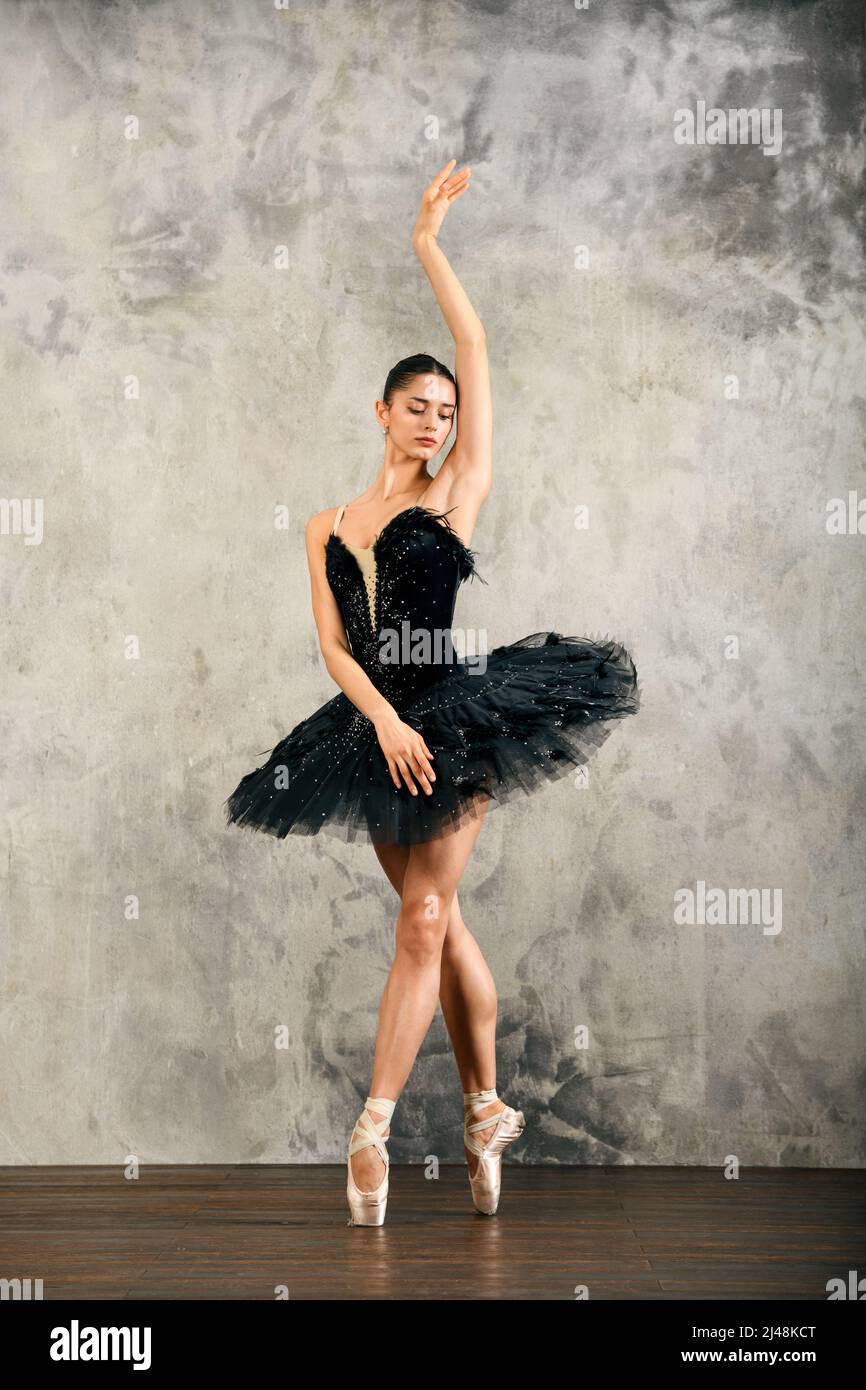 Full Body schlanke Ballerina im schwarzen Schwan Kostüm stehen auf pointe Shore beim Tanzen mit erhobenem Arm in Lichtstudio Stockfoto