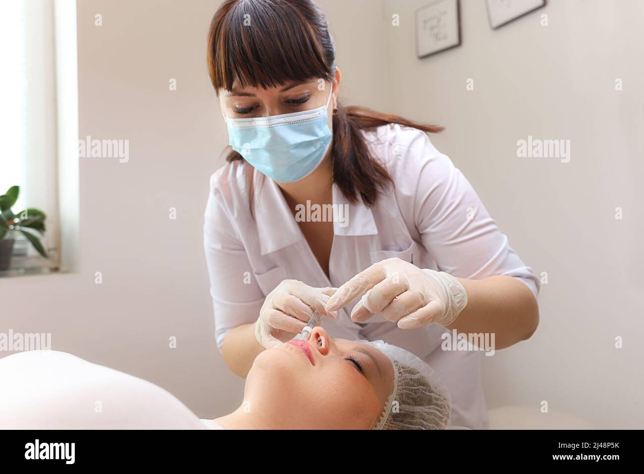 Der Kosmetologe lehnt sich über den Klienten und macht Injektionen in die Lippen mit Hyaluronsäure, um sie zu erhöhen Stockfoto