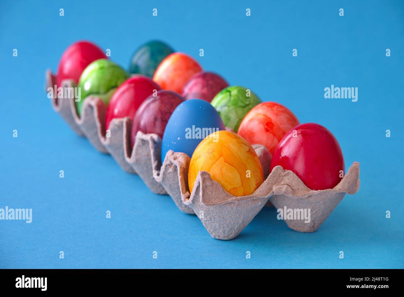 Bunte Ostereier in Pappkarton auf blauem Hintergrund Stockfoto