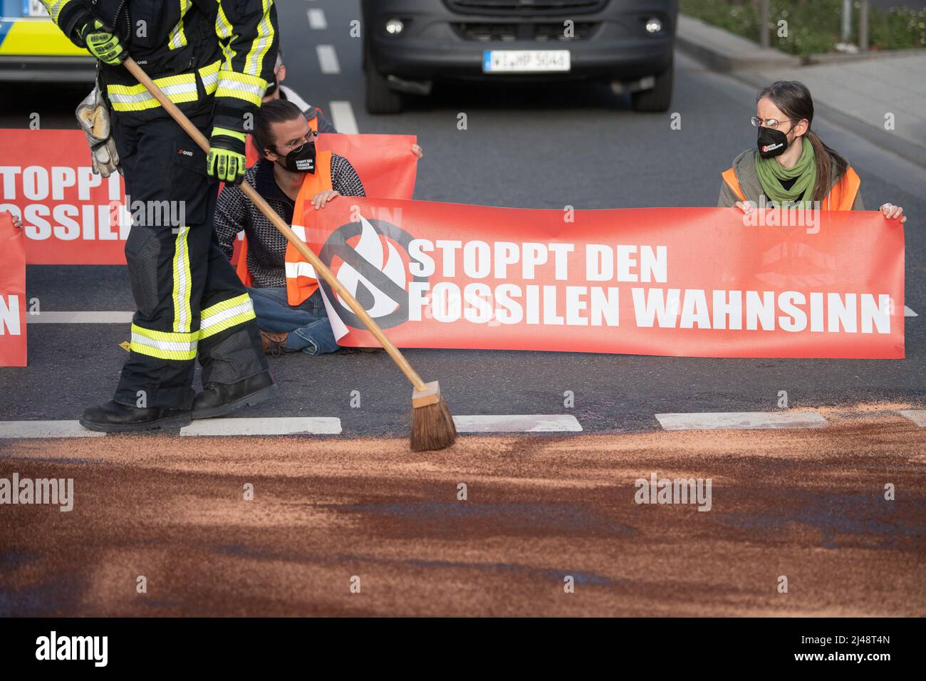 13. April 2022, Hessen, Frankfurt/Main: Ein Feuerwehrmann fegt bei einem Protest der Gruppe „Letzte Generation“ in der Nähe der Autobahn A661 Bindemittel, das über eine Mischung aus Wasser und Farbe gegossen wurde, nach oben. Unter anderem fordert die Gruppe einen Stopp aller Investitionen in den Ausbau der Infrastruktur, die zur Bereitstellung fossiler Brennstoffe dient. Foto: Sebastian Gollnow/dpa Stockfoto