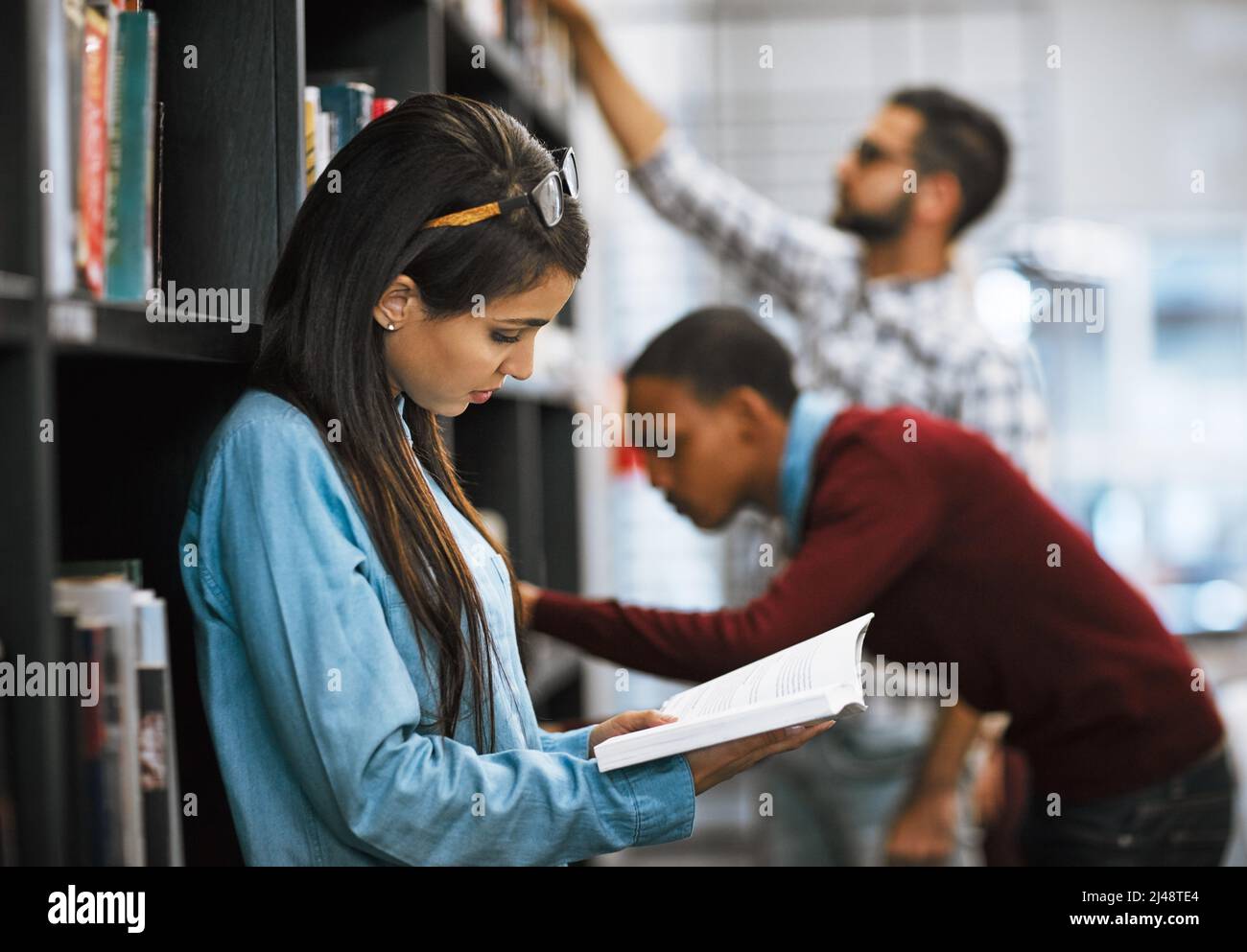 Ich kann dieses Buch nicht niederlegen. Aufnahme einer Gruppe junger Studenten, die in einer Bibliothek stehen und Bücher zum Lesen auslesen. Stockfoto