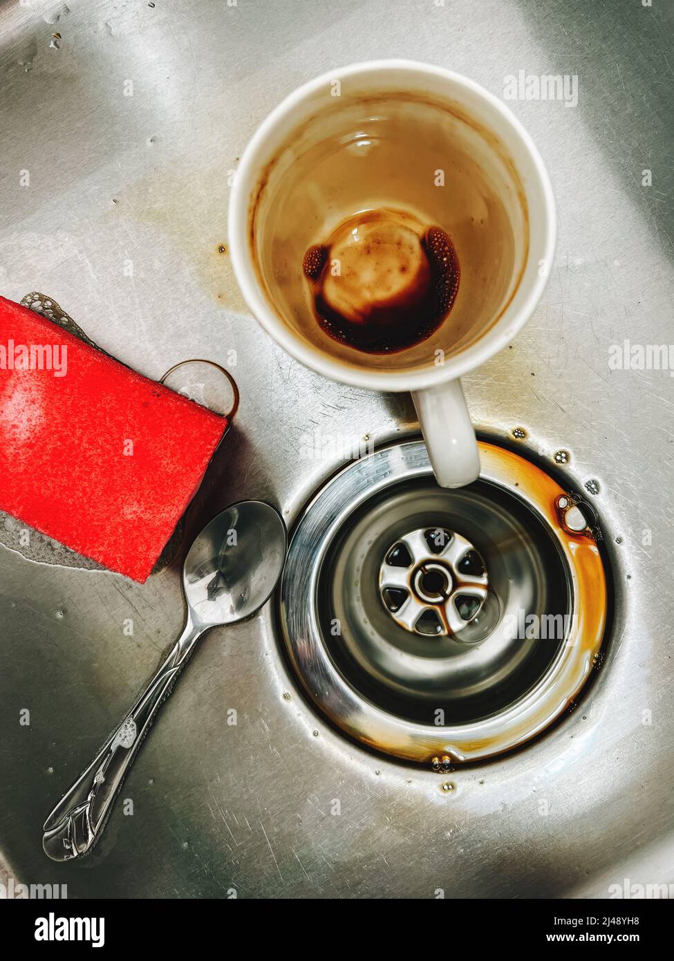 Schwamm, Kaffeetasse und ein Teelöffel im Spülbecken, Draufsicht Stockfoto
