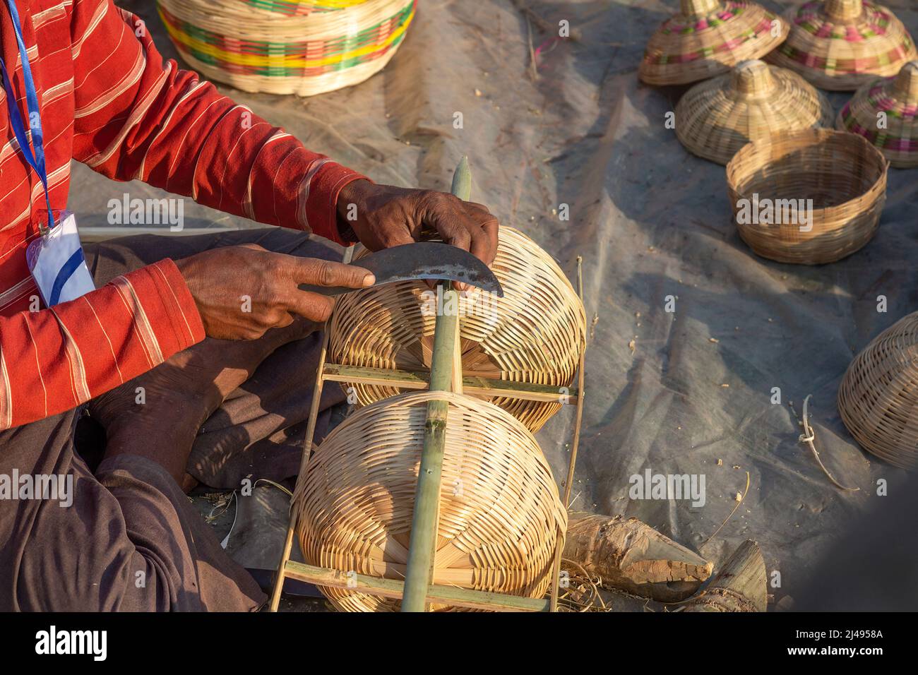 Ländlicher indischer Handwerker, der Bambusstäbchen mit Sichel für die Herstellung von Möbelstücken auf einer Kunsthandwerksmesse in Kalkutta, Indien, schneidet Stockfoto