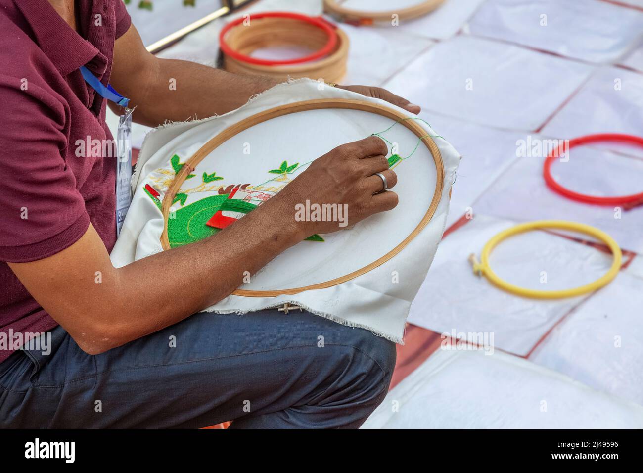 Ein Mann, der Stickereien an weißen Bettlaken macht, die auf der Kunsthandwerksmesse in Kalkutta, Indien, verkauft werden. Stockfoto