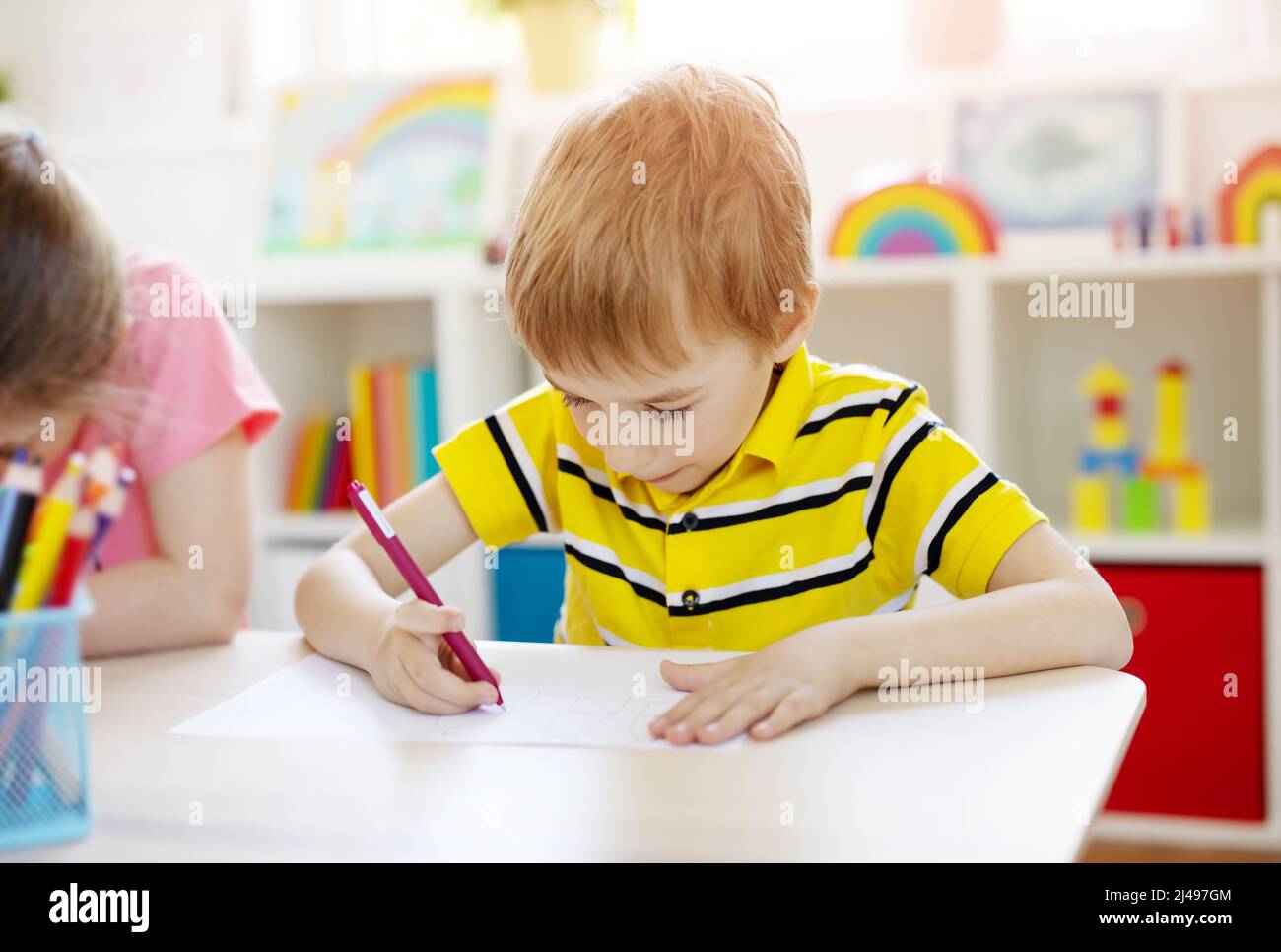 Schuljunge im Klassenzimmer sitzt an den Tischen und schreibt eine Lektion. Stockfoto