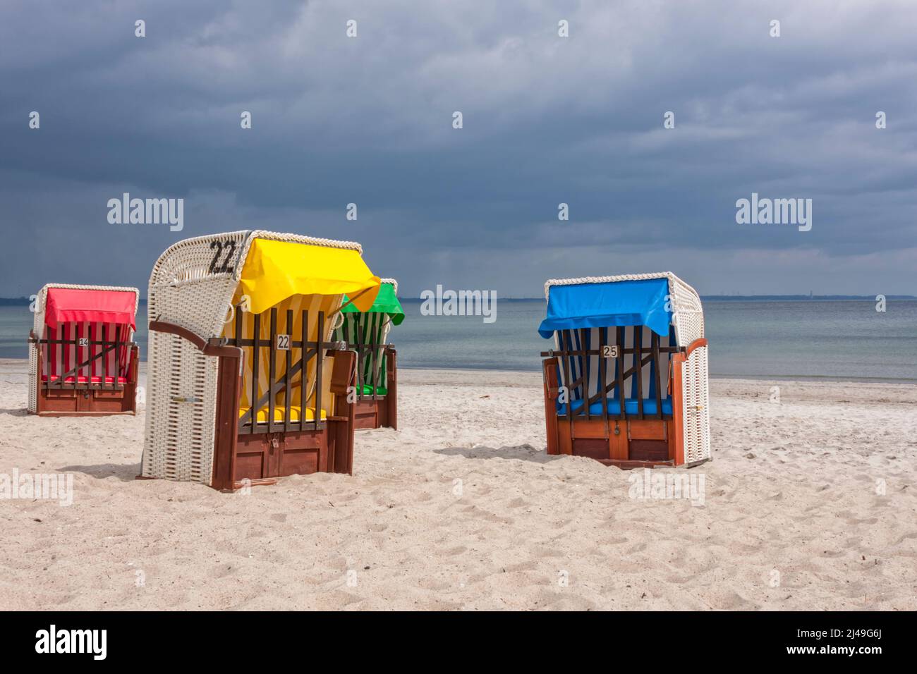 Vier Liegestühle mit Kapuze in lebendigen Farben am Ostseestrand, strahlende Sonne, dunkle Regenwolken Stockfoto