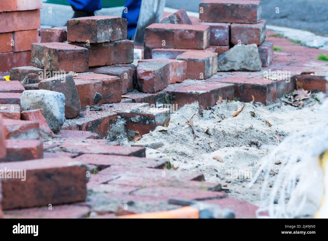 Infrastrukturreparatur an einem Bürgersteig oder Bürgersteig, der gepflastert und repariert werden muss, wobei ein Loch mit Sand und einer Gruppe roter Ziegelsteine angezeigt wird Stockfoto