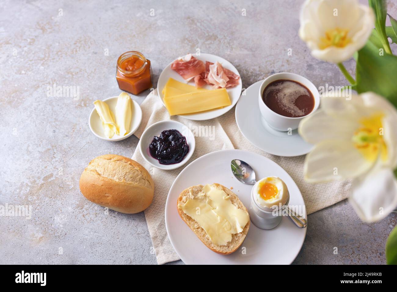 Frühstück mit herzhaften und süßen Zutaten, Brötchen, Ei, Kaffee und Blumen auf hellem Steingrund, Kopierraum, Blick von oben, ausgewählter Fokus, Stockfoto