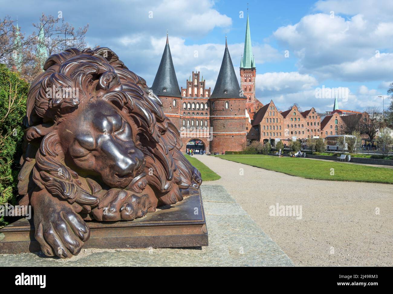 Schlafende Löwenskulptur aus Eisen vor dem Holstentor oder Holstentor, dem Wahrzeichen der historischen hansestadt Lübeck in Deutschland, blau s Stockfoto