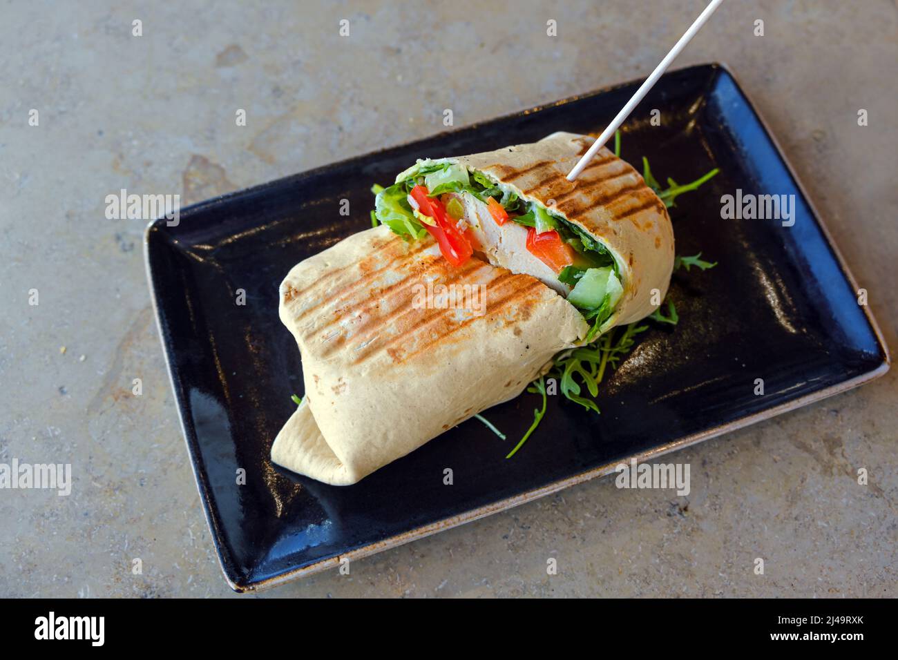 Tortilla Wrap gefüllt mit Huhn und Gemüse auf einem schwarzen Teller und einem Marmortisch, mexikanisches Essen, Kopierraum, ausgewählter Fokus, enge Schärfentiefe Stockfoto
