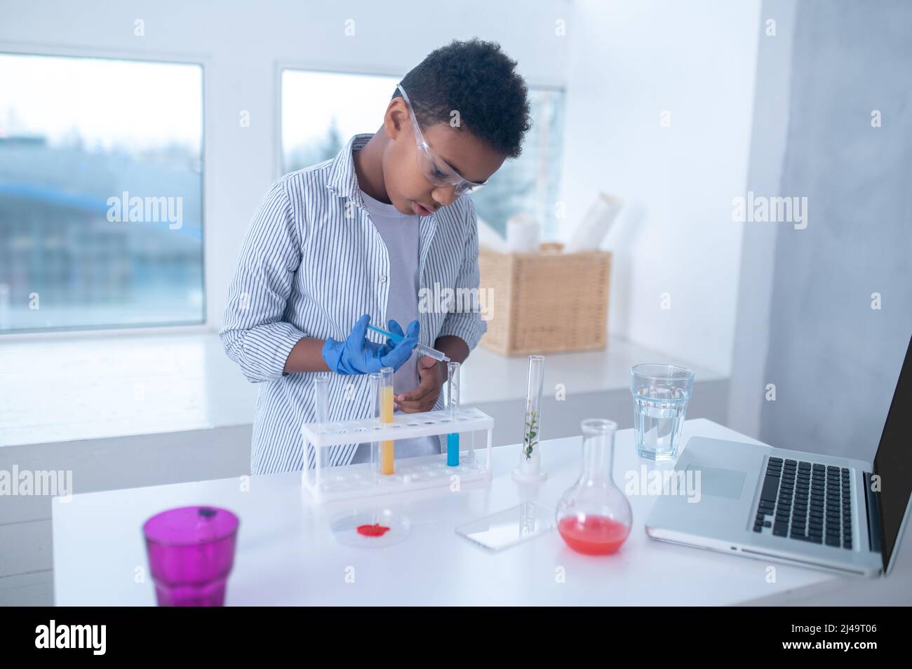 Ein dunkelhaariger Junge in einem Labormantel, der während eines chemischen Experiments beschäftigt aussieht Stockfoto