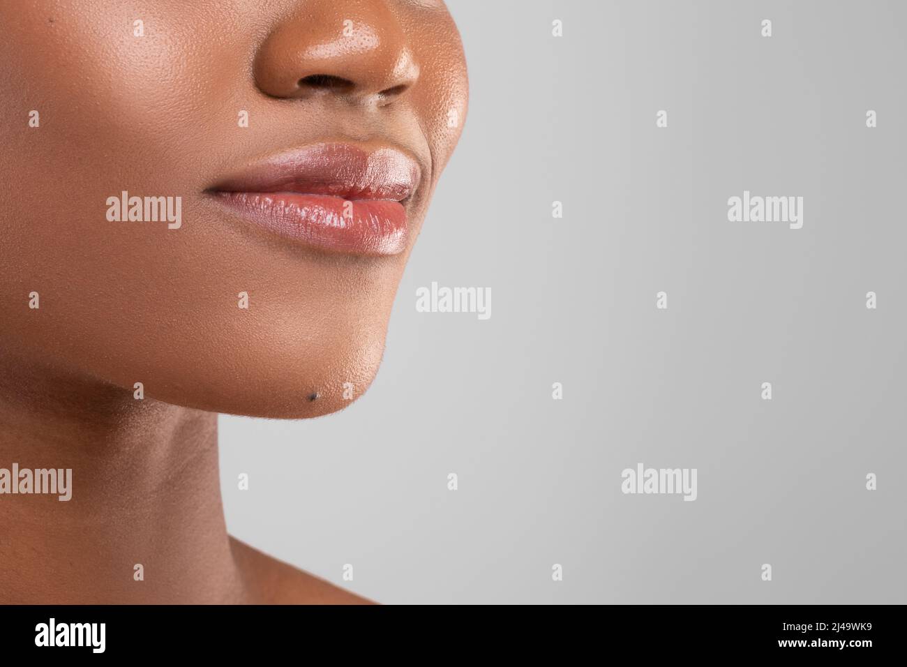 Lächelnde Lippen der hübschen tausendjährigen afroamerikanischen Dame mit perfekter Haut isoliert auf grauem Hintergrund, Nahaufnahme Stockfoto