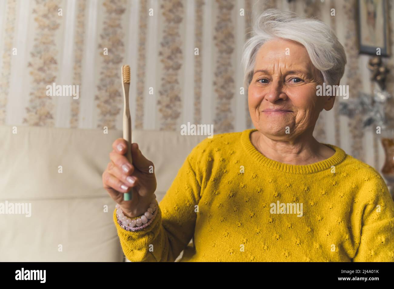 Senioren wählen Ökologie. Freundliche, glückliche kaukasische, grauhaarige Großmutter, die eine ökologische Bambuszahnbürste in der Hand hält und die Kamera anschaut. Hochwertige Fotos Stockfoto