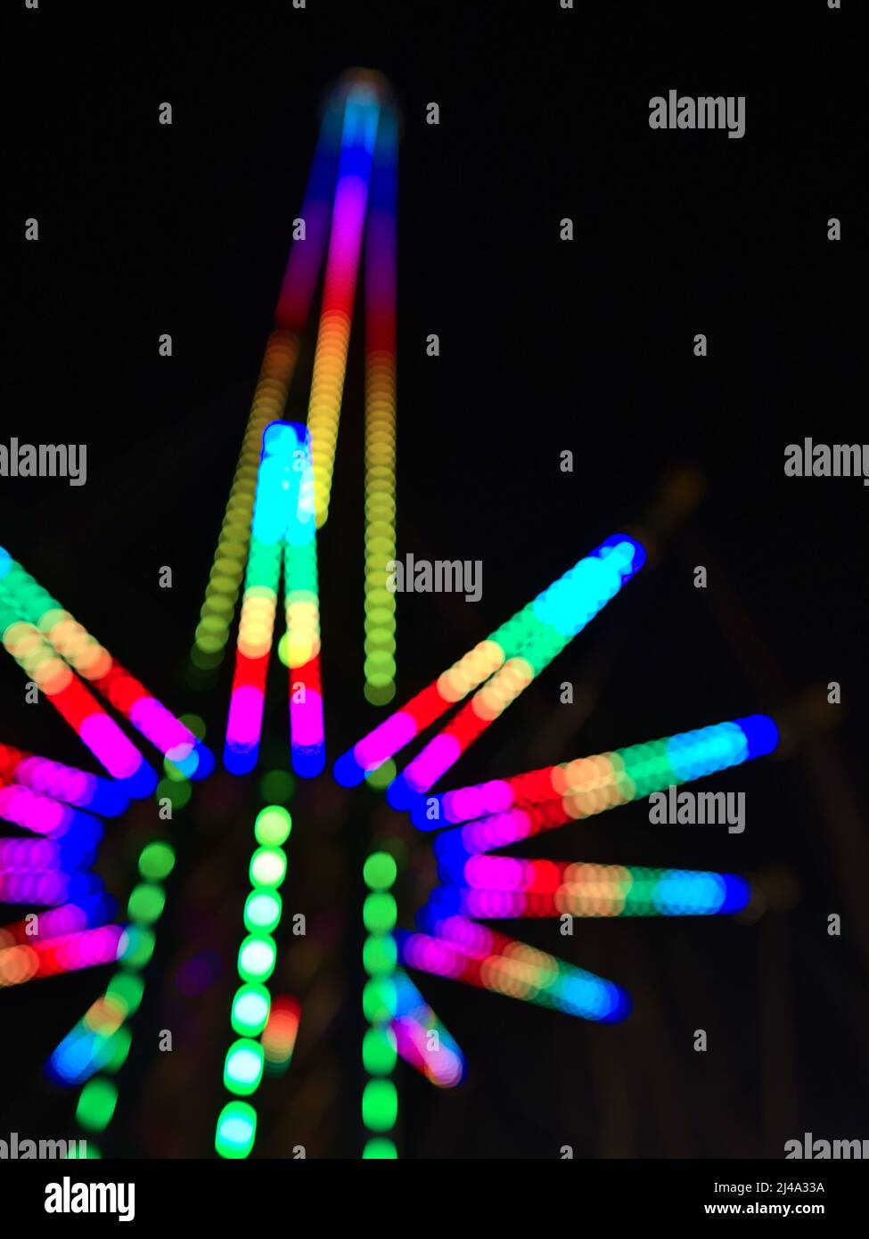 Defokussierte (verschwommene) Ansicht eines großen Fallturms mit beleuchteter Struktur bei Nacht im Vergnügungspark Wurstelprater in der Nähe des Wiener Praters, Wien, Österreich. Stockfoto