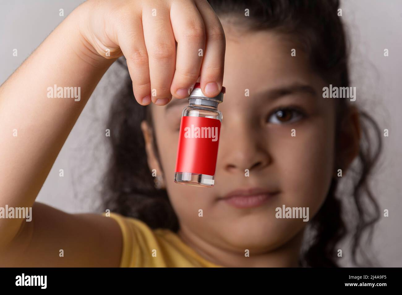 Kleines Mädchen, das eine Injektionsfläschchen vor dem Gesicht hält. Bearbeitbare Modell-up-Serie Vorlage bereit für Ihr Design. Flasche Etikett Auswahlpfad enthalten. Stockfoto