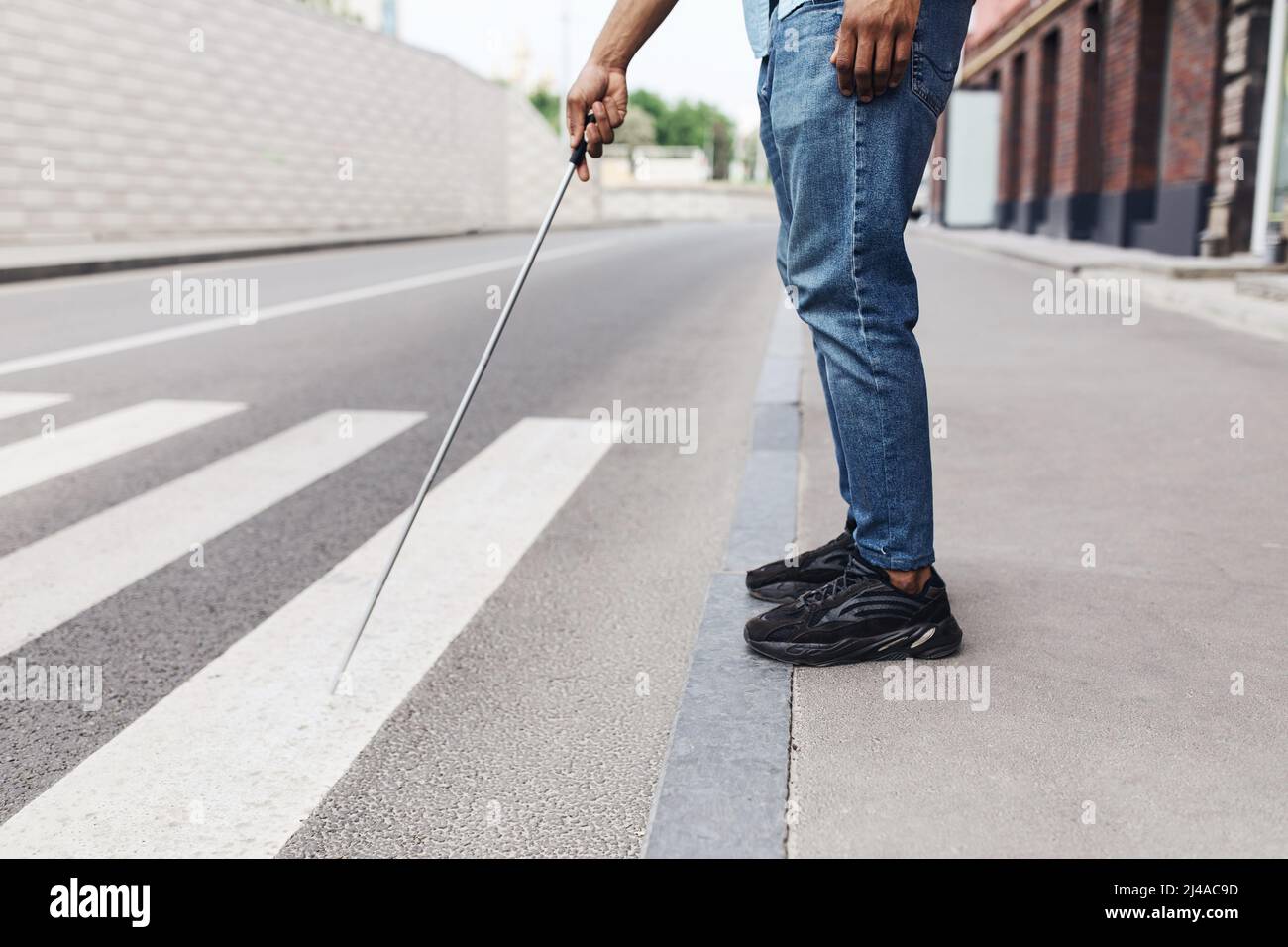 Beschnittene Ansicht eines jungen schwarzen Mannes mit Sehbehinderung, der am Straßenrand steht, mit Gehstock im Stadtzentrum, Platz kopieren Stockfoto