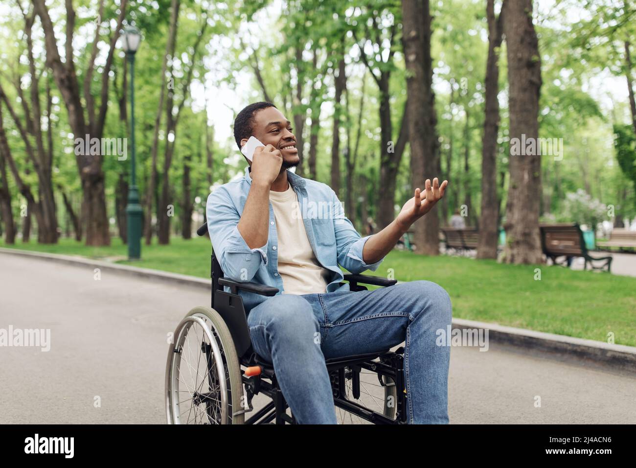 Junger schwarzer Mann im Rollstuhl, der im Sommer Telefongespräche im Stadtpark führt Stockfoto