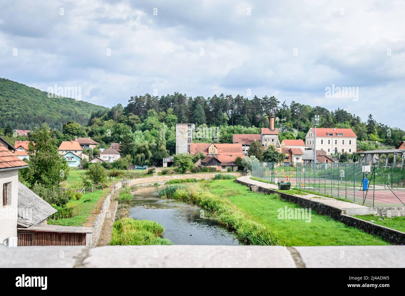 Panoramablick auf ein Dorf in der Landschaft von Kroatien im Herbst. Traditionelle Hütten, Fluss & Sportanlagen vor einem Hügel mit Wald Stockfoto