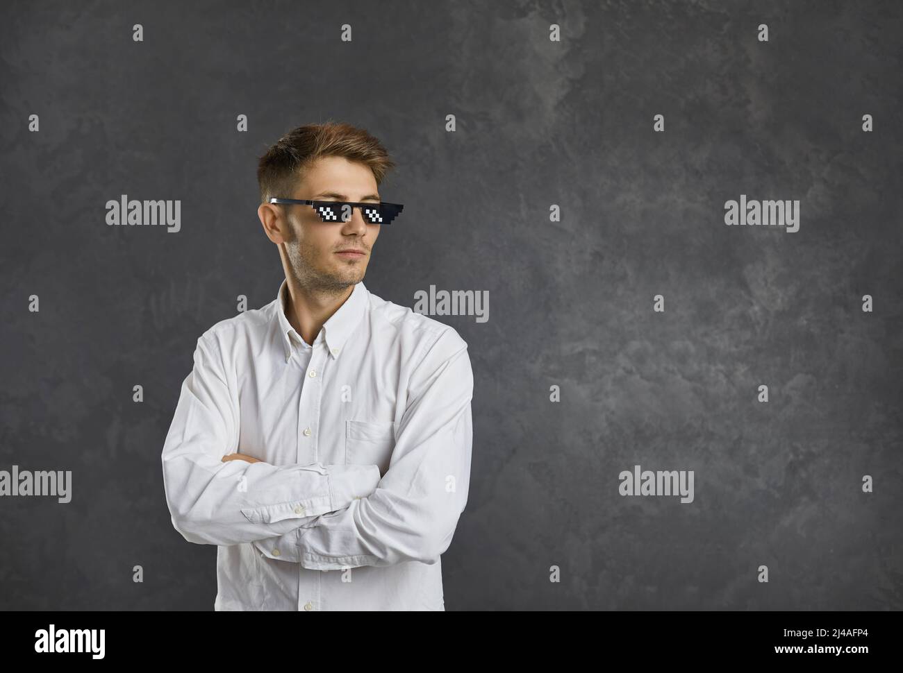 Selbstbewusster junger Mann in einer Strolch-Lebensbrille, der vor grauem Hintergrund des Kopierraums steht Stockfoto