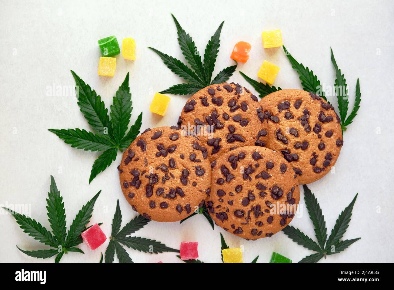 Amerikanische Cookies mit Cannabisextrakt. Süßigkeiten mit CBD-Öl. Marihuana Blätter auf weißem Hintergrund. Draufsicht, flach liegend. Stockfoto
