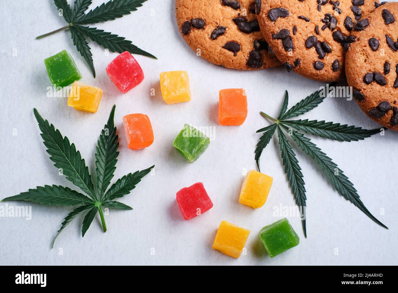 Marmelade und amerikanische Kekse mit Cannabisextrakt. Süßigkeiten mit CBD-Öl. Marihuana Blätter auf weißem Hintergrund. Draufsicht, flach liegend. Stockfoto