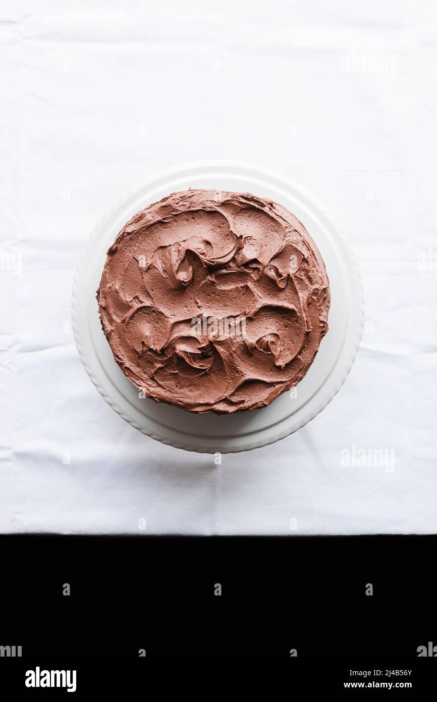 Ganze Schokoladenkuchen mit Buttercreme, auf weißem Kuchenständer. Stockfoto
