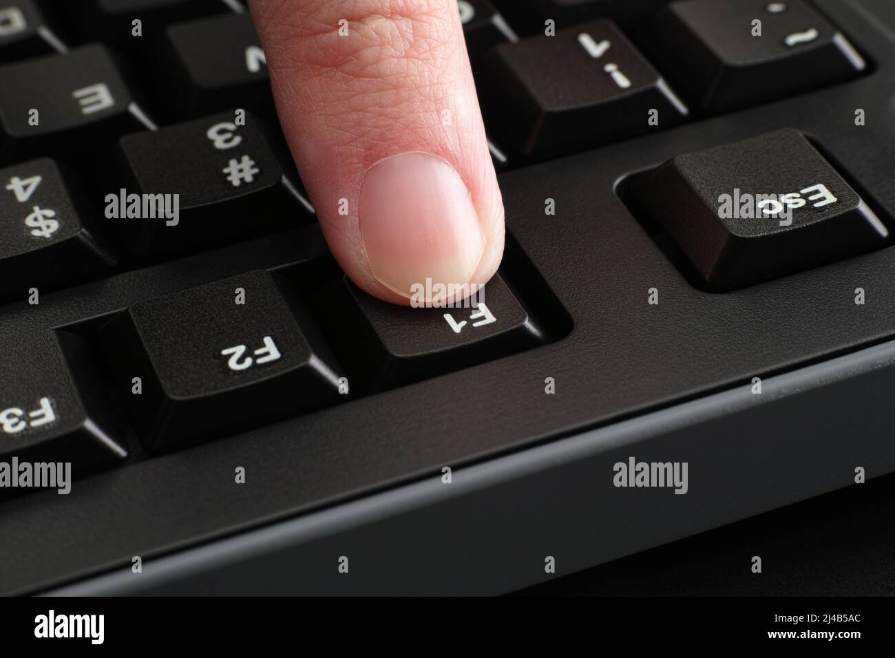 Ein Finger, der die F1-Taste auf einer schwarzen Computertastatur drückt. Nahaufnahme. Stockfoto