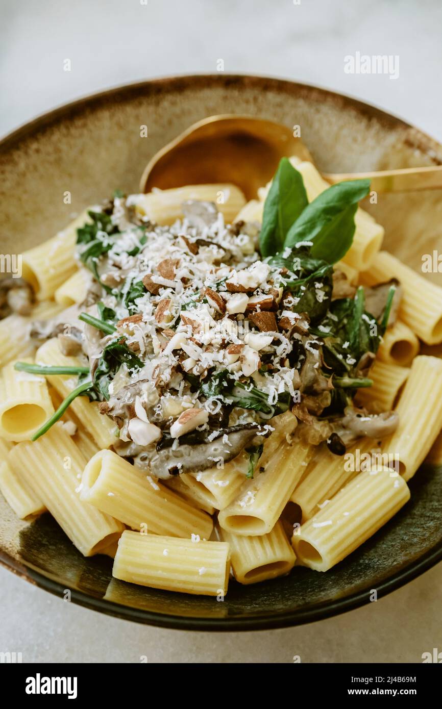 Nahaufnahme eines Rigatoni-Nudeltellers, mit Rahm, Pilz, Spinat, Mandel und geriebenem Parmesan, in handgefertigten Tellern, auf einem Marmortisch Stockfoto