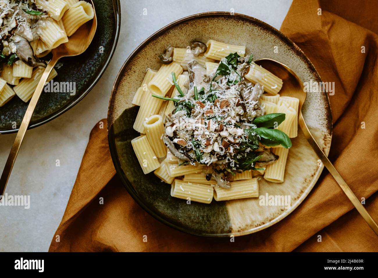 Draufsicht auf Rigatoni Nudelgericht, mit Creme, Pilz, Spinat, Mandel und geriebenem Parmesan, in handgefertigten Tellern, und Glas Weißwein, auf einem Marmor-T Stockfoto