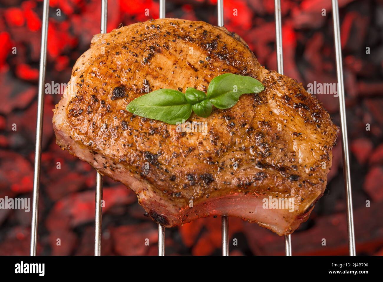 Frisches Steak aus Schweinefleisch mit Basilikum auf einem Grill unter brennender Kohle Stockfoto