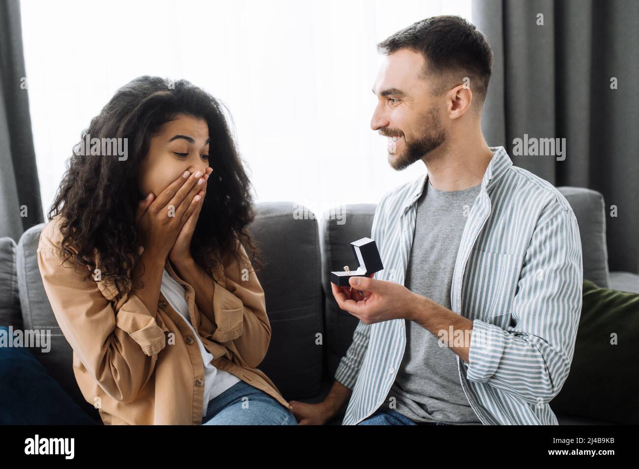 Heiratsantrag. Eine Überraschung für die geliebte Frau. Ein Kerl gibt seinem geliebten afroamerikanischen Mädchen einen Verlobungsring, sie nimmt ihn gerne an. Glückliches Paar in der Liebe Stockfoto
