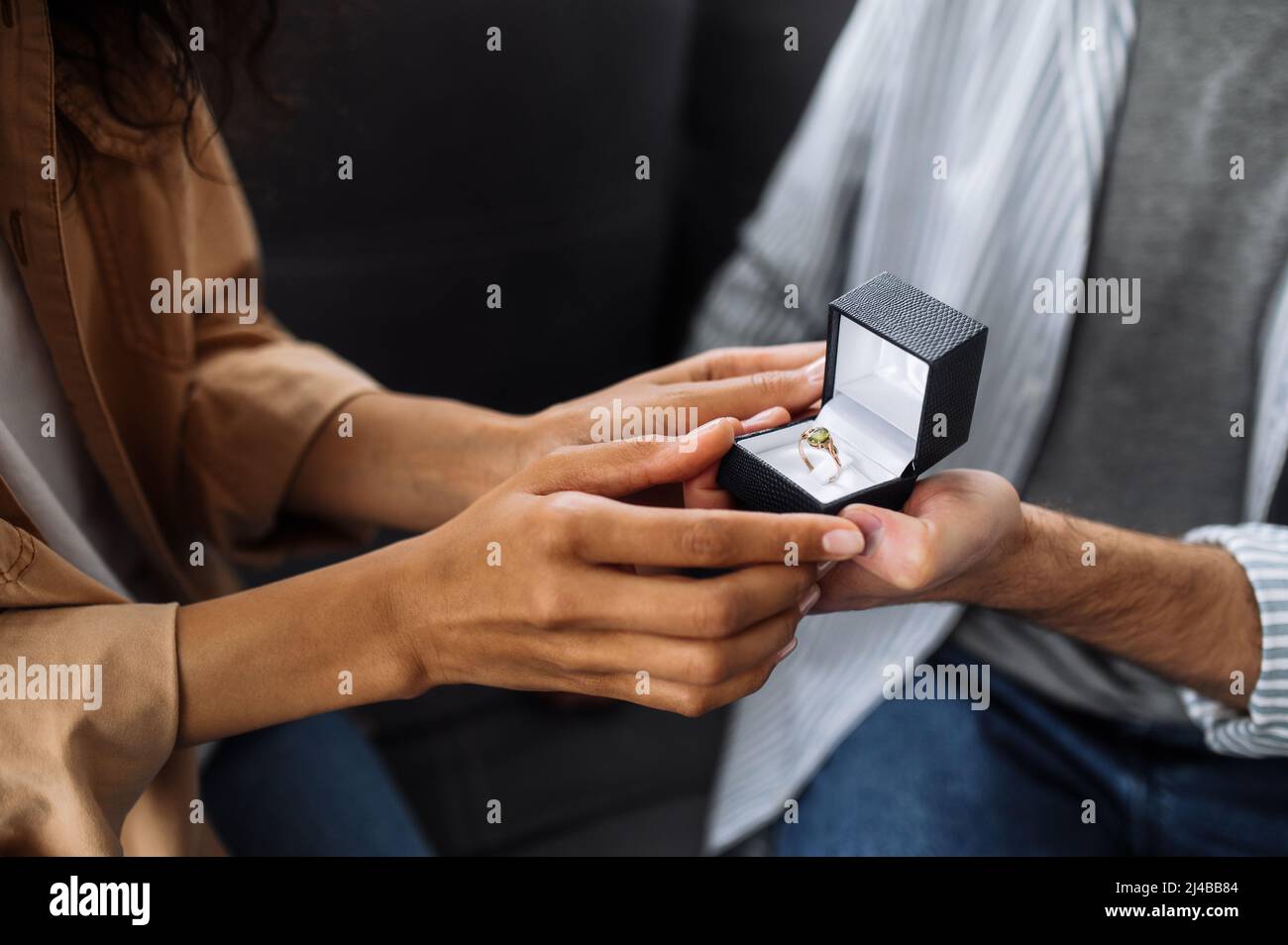 Nahaufnahme eines kaukasischen Mannes gibt seiner geliebten afroamerikanischen Frau einen Verlobungsring, den sie gerne annimmt Stockfoto