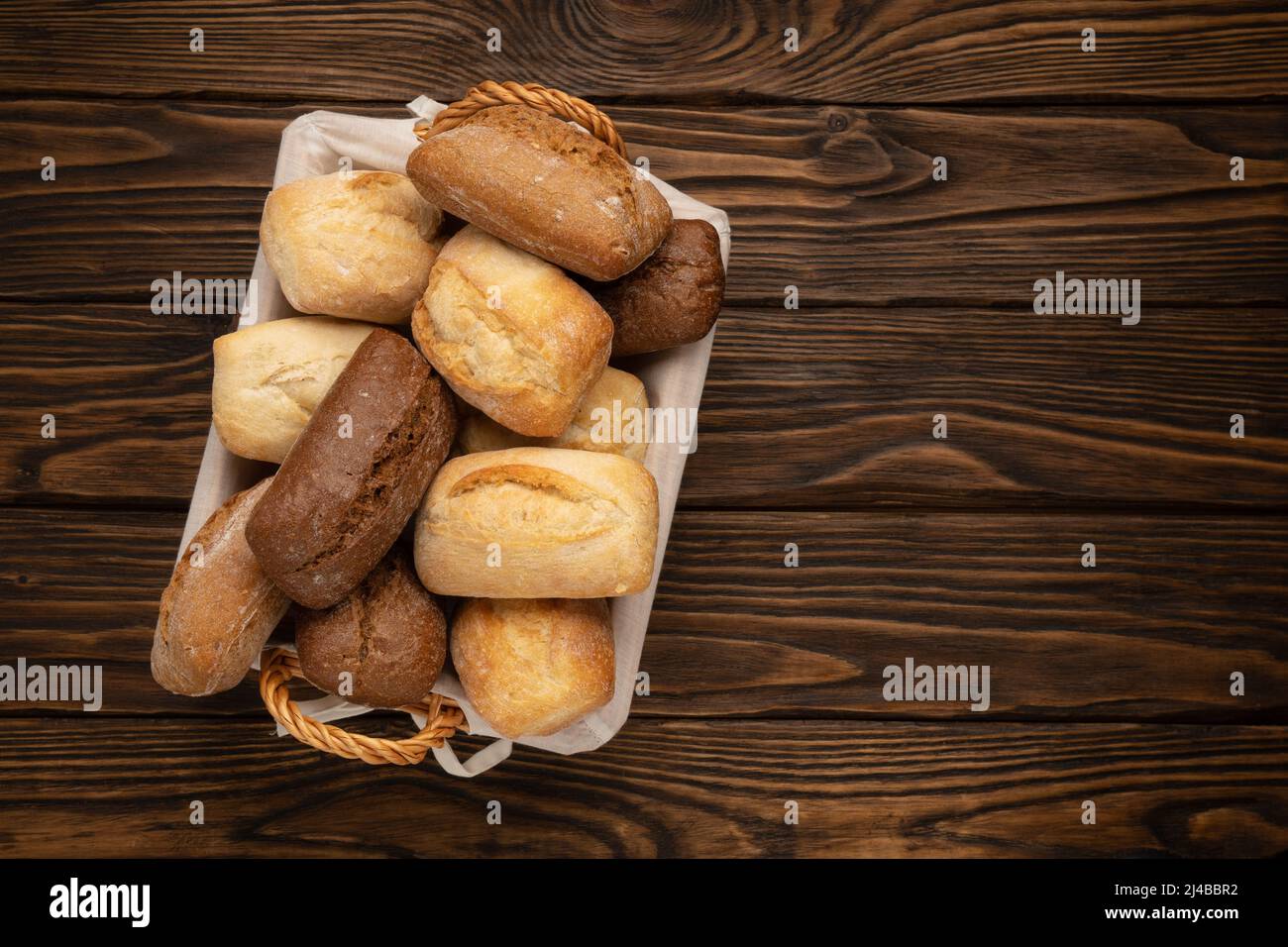 Frisches Weizen- und Roggenbrot in einem Korbkorb auf einem braunen Holztisch Stockfoto