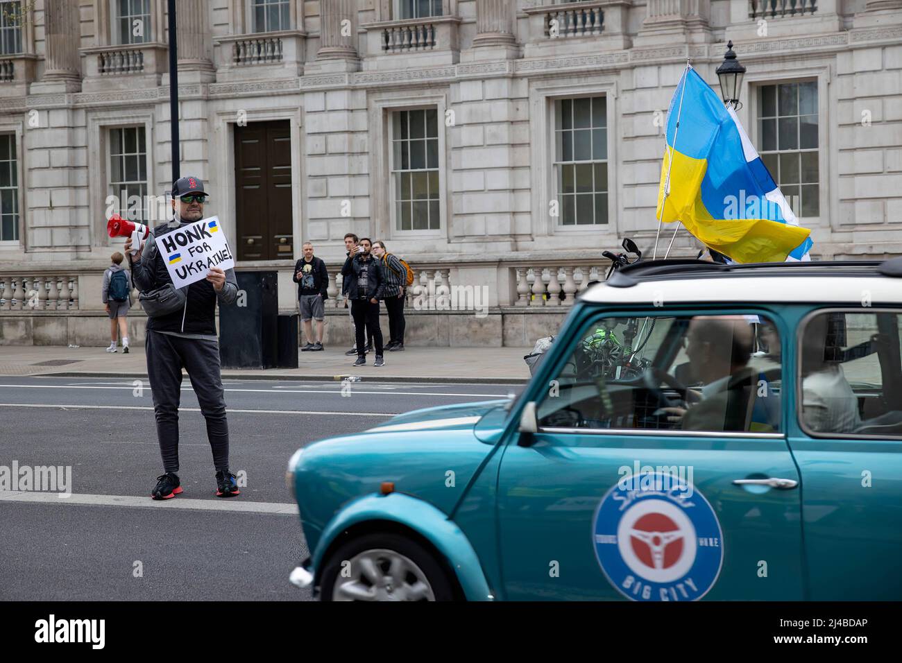 London, Großbritannien. 13. April 2022. Ein Protestler hält ein Schild, auf dem die Fahrer aufgefordert werden, die Ukraine während der Fahrt durch Whitehall zu hupen und zu unterstützen. Ukrainische Unterstützer versammeln sich täglich in Central London, um gegen die russische Invasion in der Ukraine seit dem 24.. Februar 2022 zu protestieren. Sie fordern weiterhin von der NATO, den Luftraum über der Ukraine zu schließen, um Russland daran zu hindern, das Land zu bombardieren und Waffen zur Unterstützung der ukrainischen Armee zu schicken. Kredit: SOPA Images Limited/Alamy Live Nachrichten Stockfoto