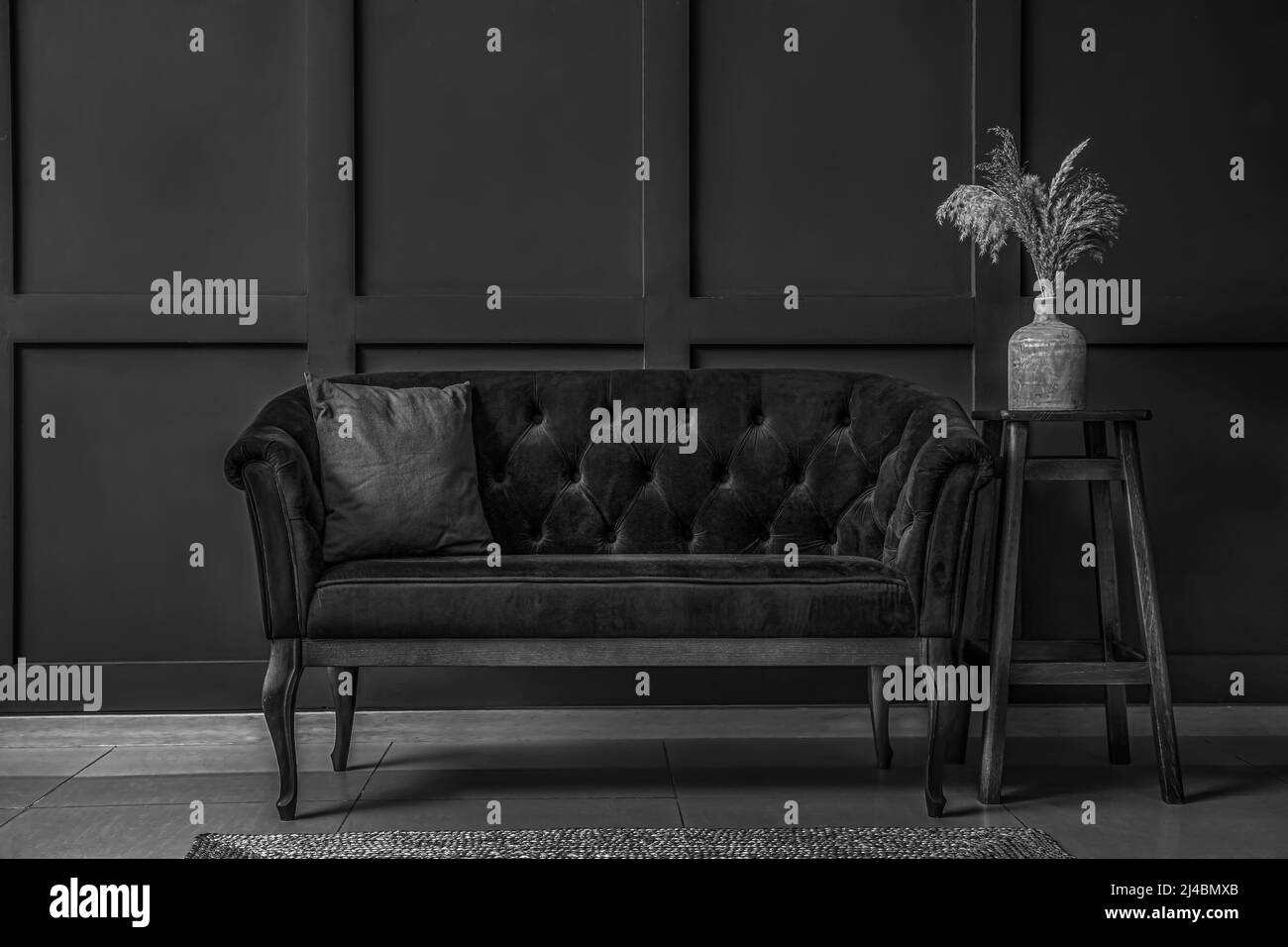 Graustufen-Foto von Wohnzimmer-Interieur mit Sofa in der Nähe der schwarzen Wand Stockfoto