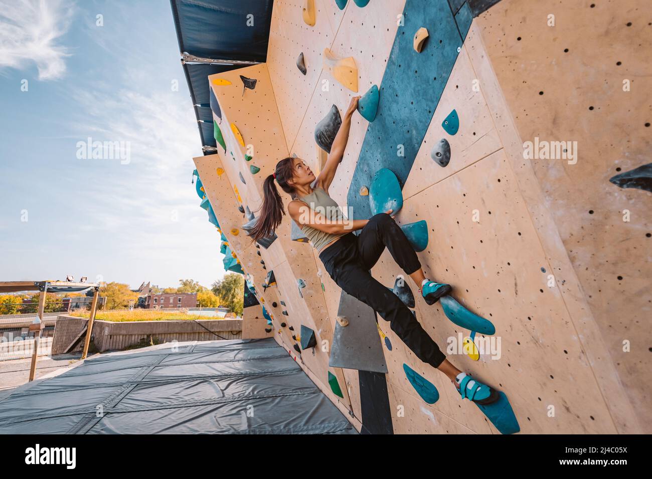 Eine Frau aus Asien klettert im Fitnessstudio an der Boulderwand im Freien hoch. Spaß aktive sportliche Aktivität Sport treiben draußen Stockfoto