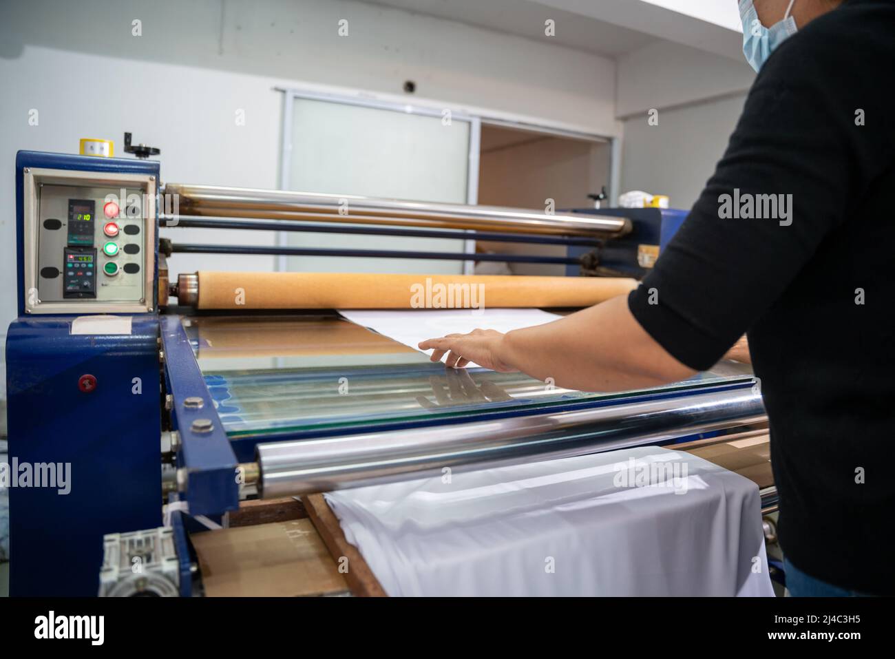 Ein Arbeiter druckt auf T-Shirt in der Werkstatt. Bekleidungsindustrie Konzept. Wärmeübertragungsmaschine. Stockfoto