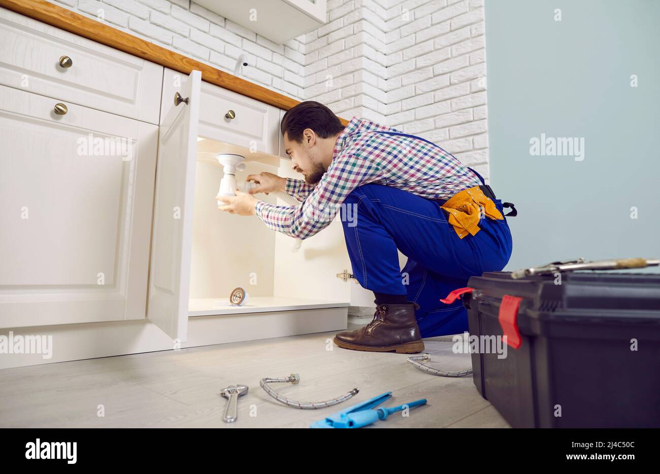 Seriöse professionelle Klempner installiert Siphon unter Waschbecken in der Küche der Wohnung. Stockfoto