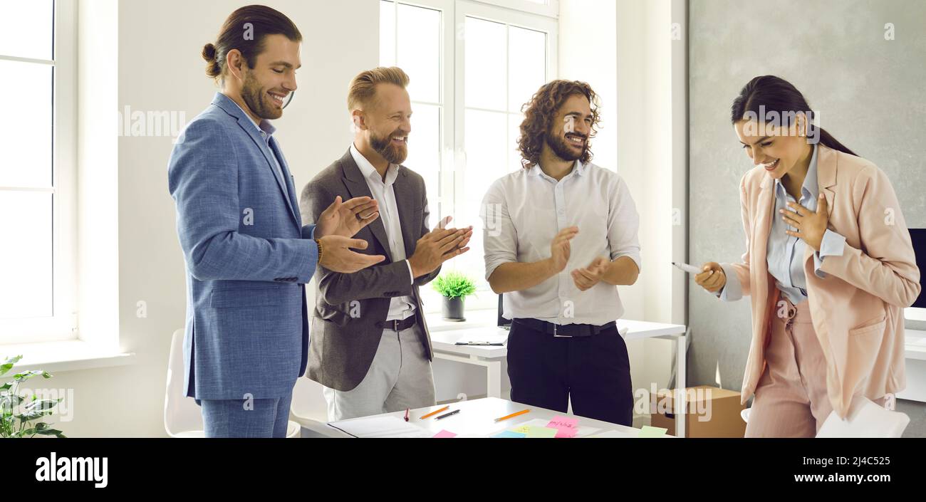 Fröhliche Geschäftsleute applaudieren ihrer Kollegin bei einem Treffen im Büro. Stockfoto