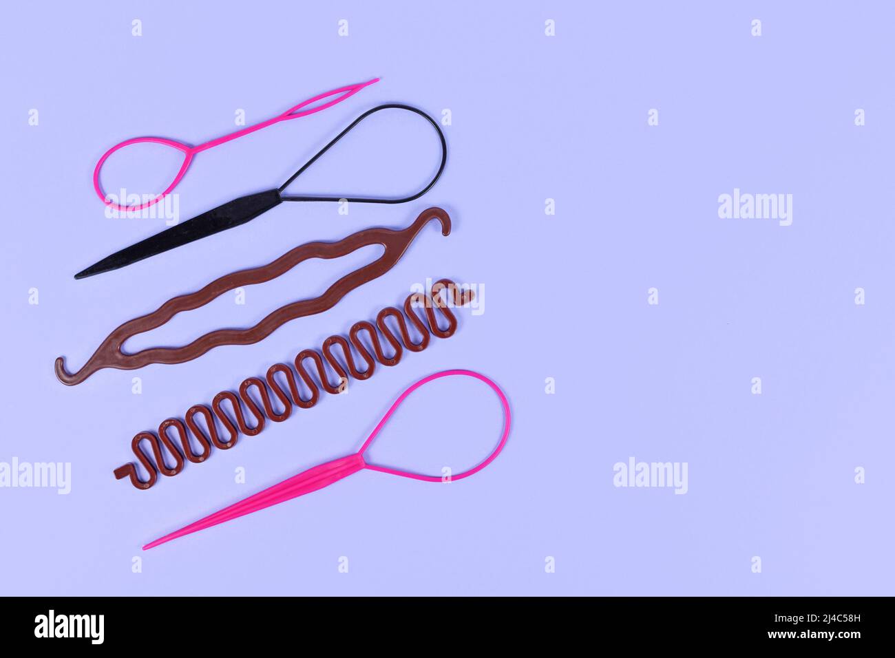 Verschiedene Haarstyling-Werkzeuge wie Bun Maker, Zopf-Werkzeug oder Pferdeschwanz-Stil Maker auf violettem Hintergrund Stockfoto