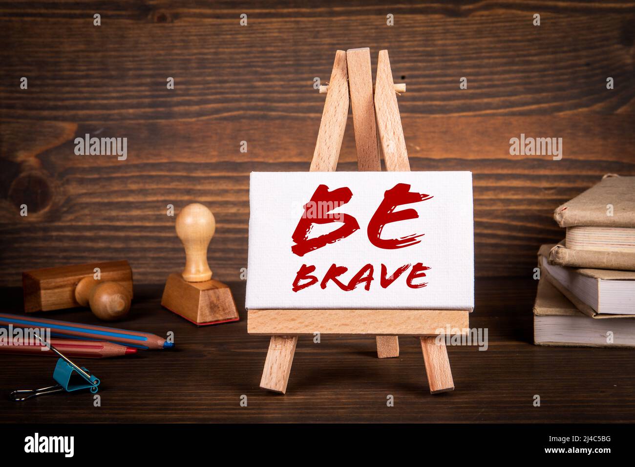 Seien Sie Mutig. Miniatur-Staffelei mit Text auf einem hölzernen Schreibtisch. Stockfoto