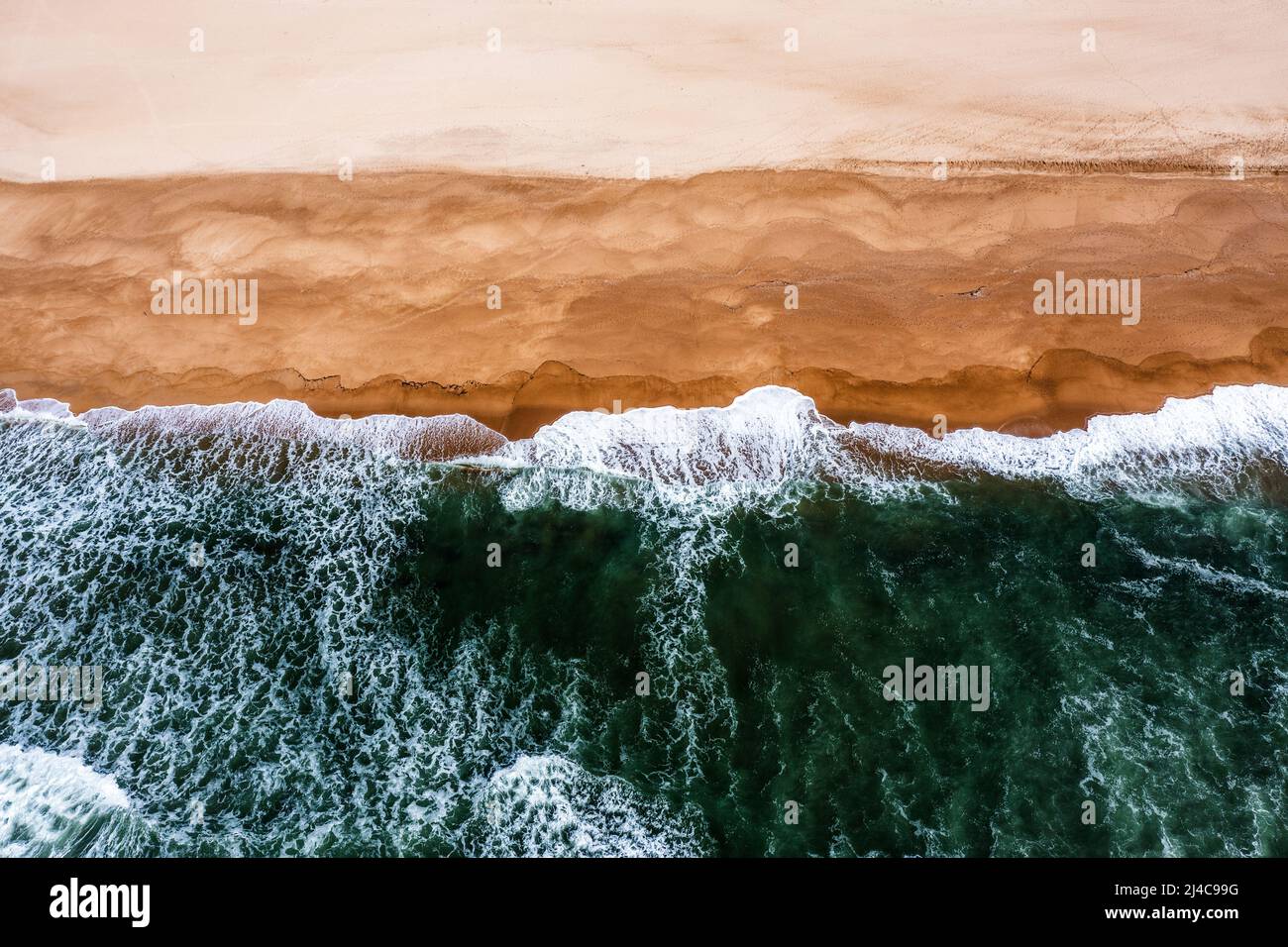 Drone-Ansicht von oben nach unten von weißgedeckten Wellen, die an einem leeren goldenen Sandstrand zusammenbrechen Stockfoto