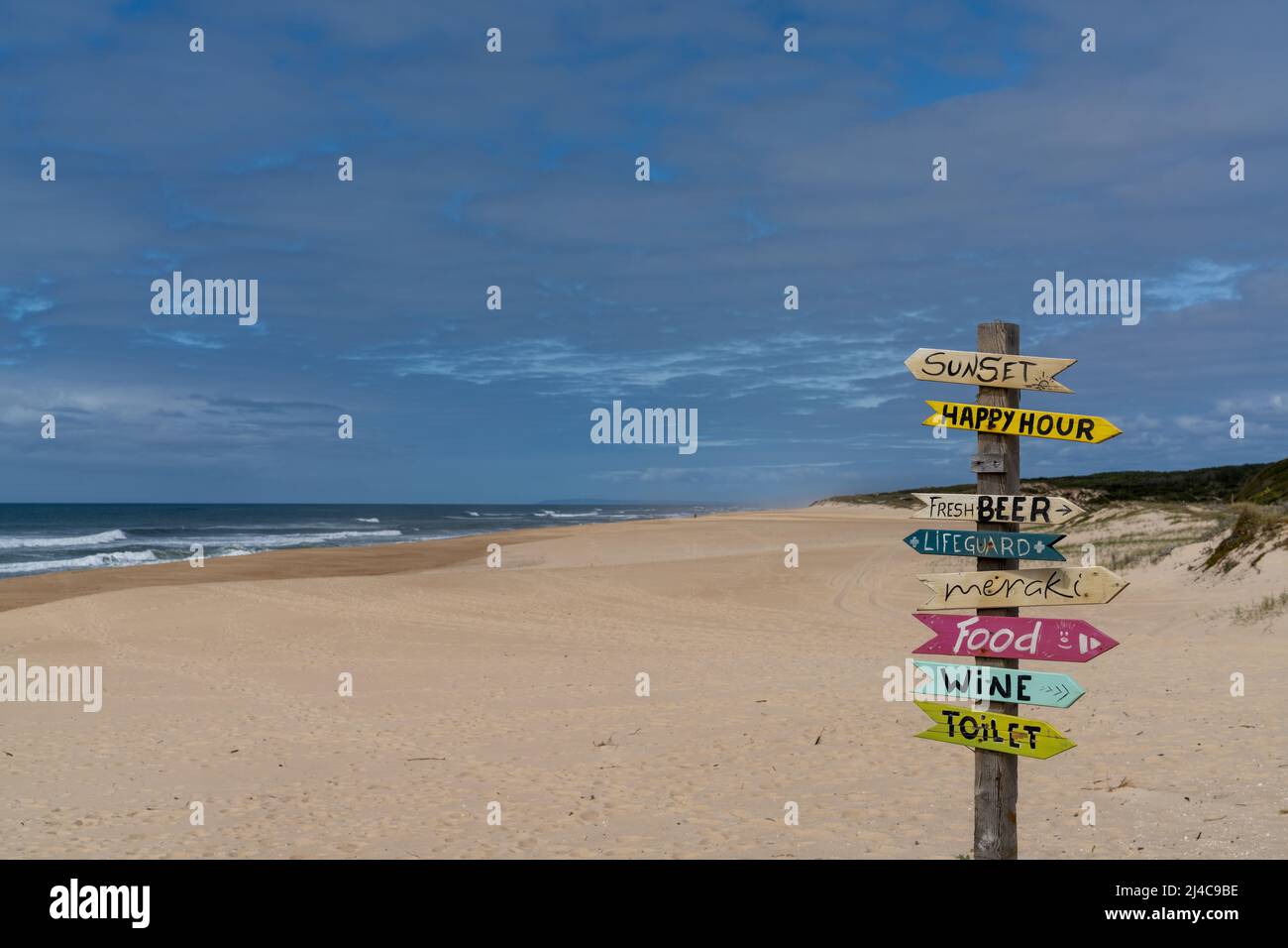 Ein malerischer leerer Strand mit bunten und humorvollen Schildern, die in verschiedene Richtungen zeigen Stockfoto