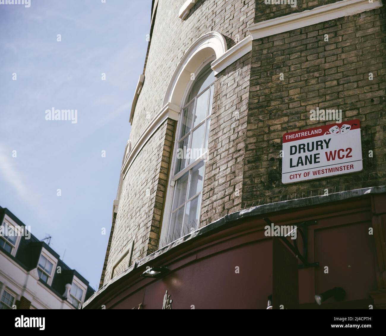 Greater London, London, Großbritannien - 12. April 2016: Ein Gebäude im Osten Londons, das vor einem klaren blauen Himmel steht, zeigt das Straßenschild der Drury Lane. Stockfoto